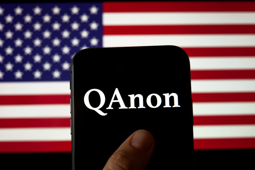 アメリカ国旗とスマートフォンに表示されたQアノンの文字